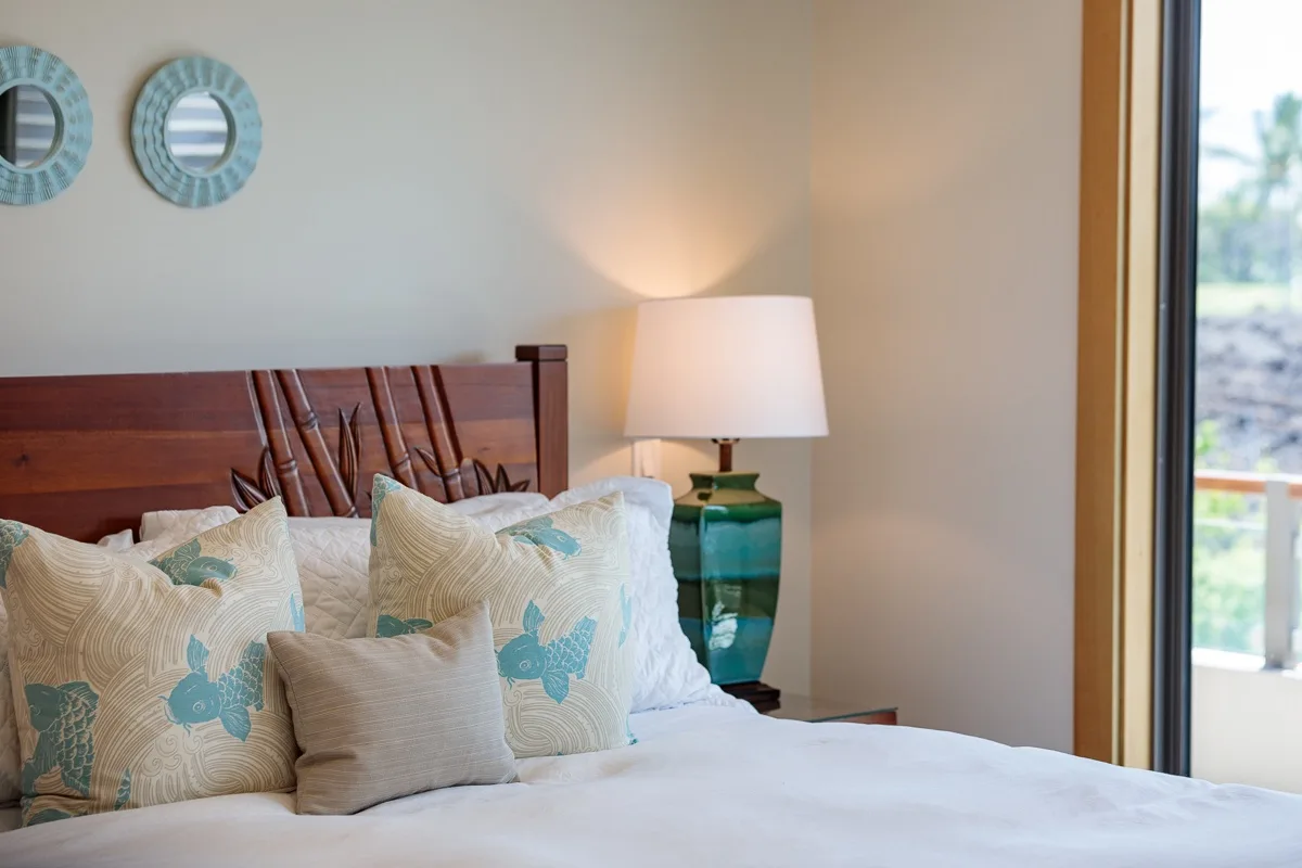 Dormitorio con cama, almohadas estampadas y una lámpara junto a una ventana grande.