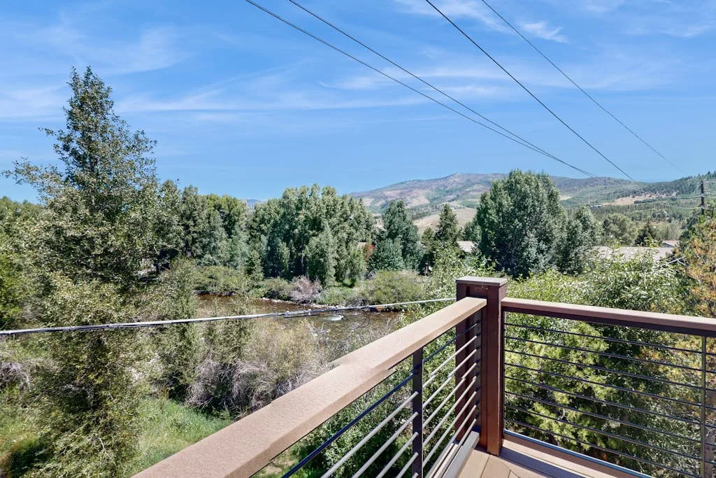 A balcony railing overlooks trees and a green valley beneath distant hills.