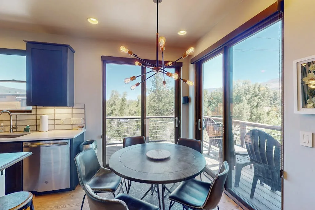 A dining area with a round table beside large glass doors overlooking trees.