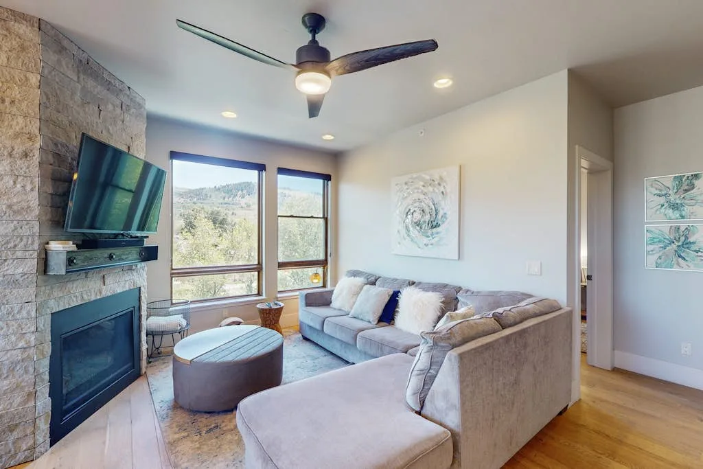 A bright living room with an L-shaped sectional and a stone fireplace.