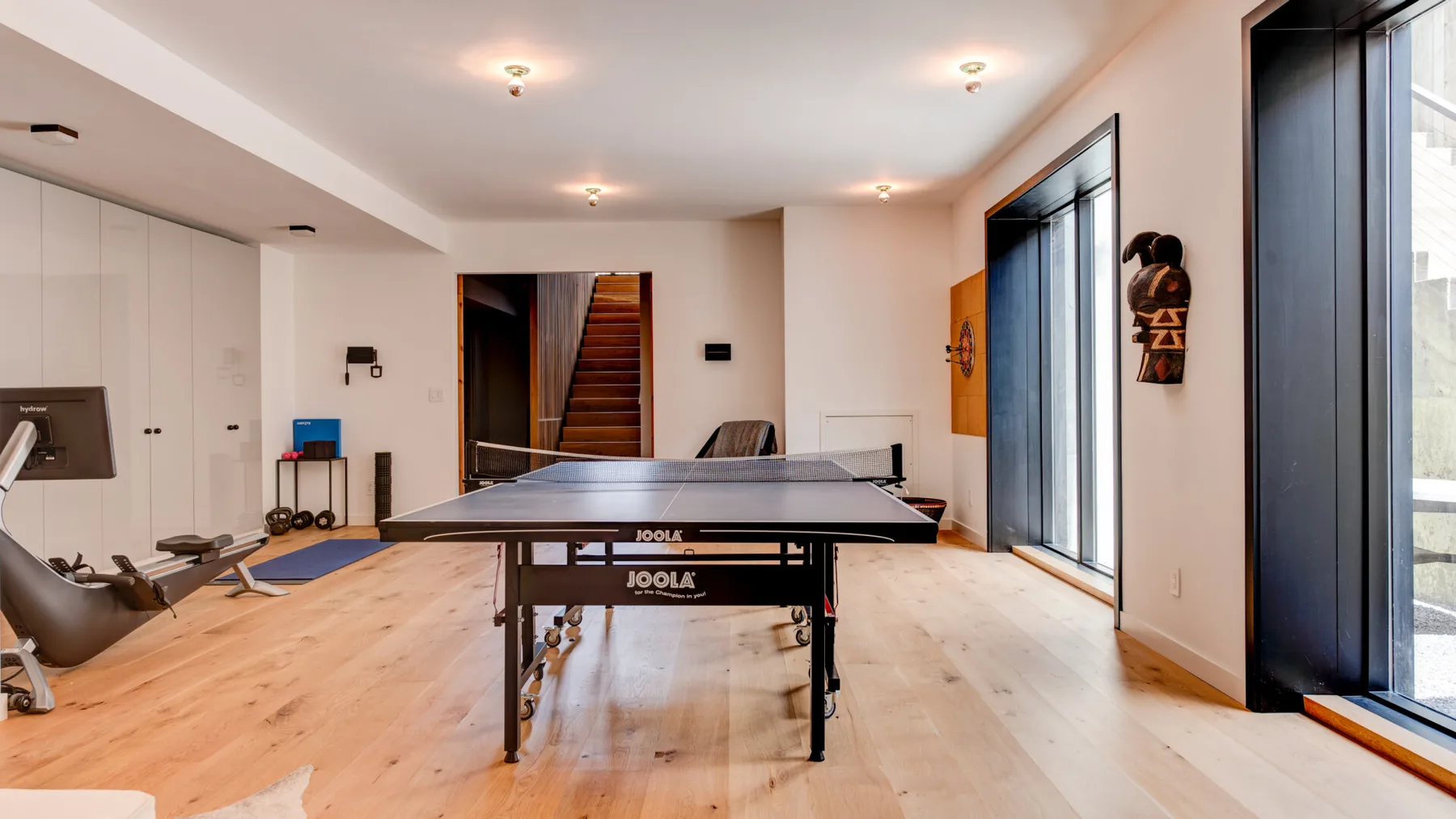 A bright recreation room features a ping-pong table and exercise equipment.