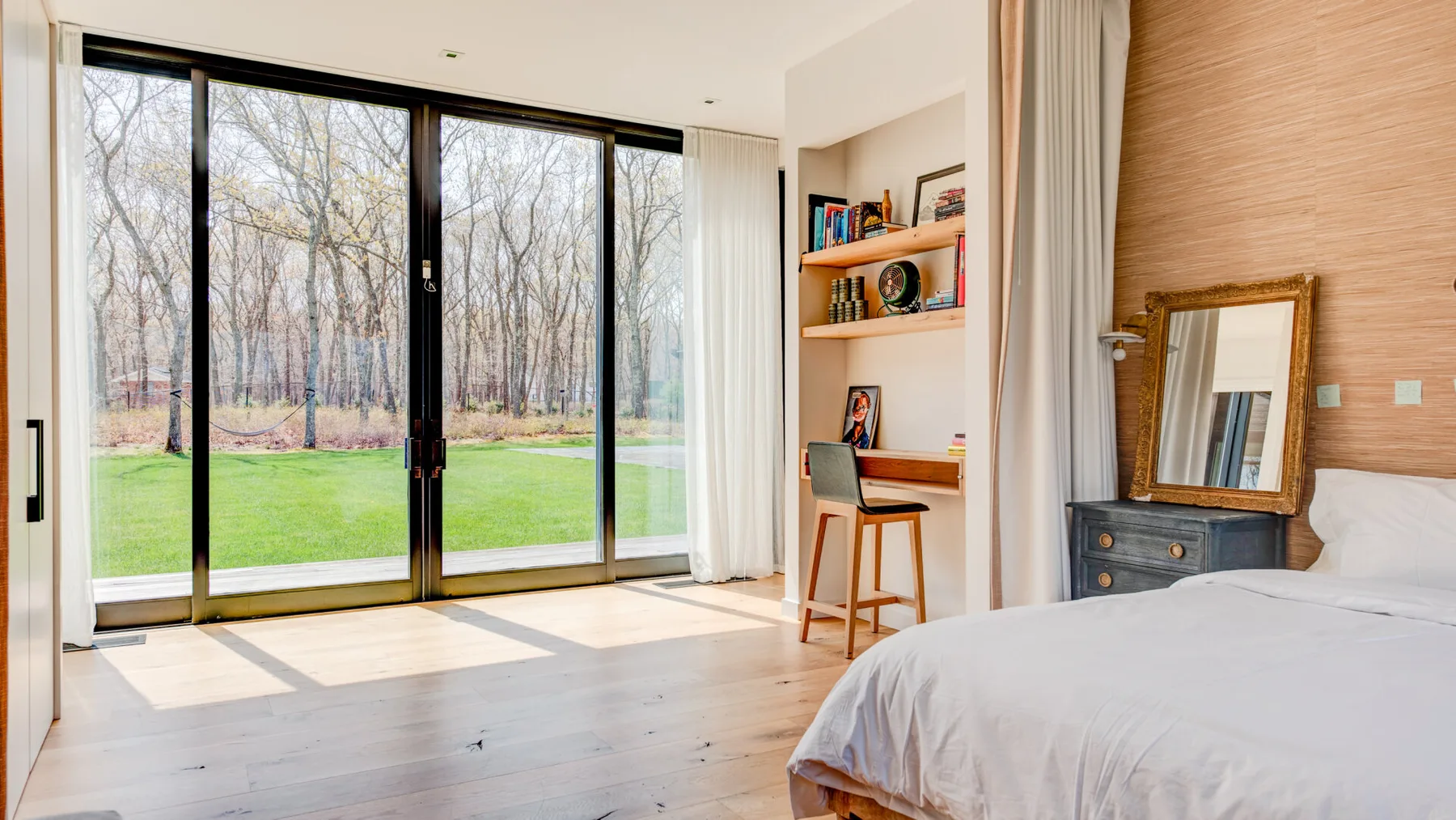 A bright bedroom with large glass doors opening onto a green lawn.