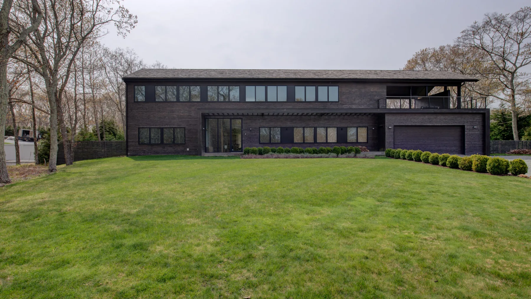A modern dark-clad house stands beyond a broad green lawn.