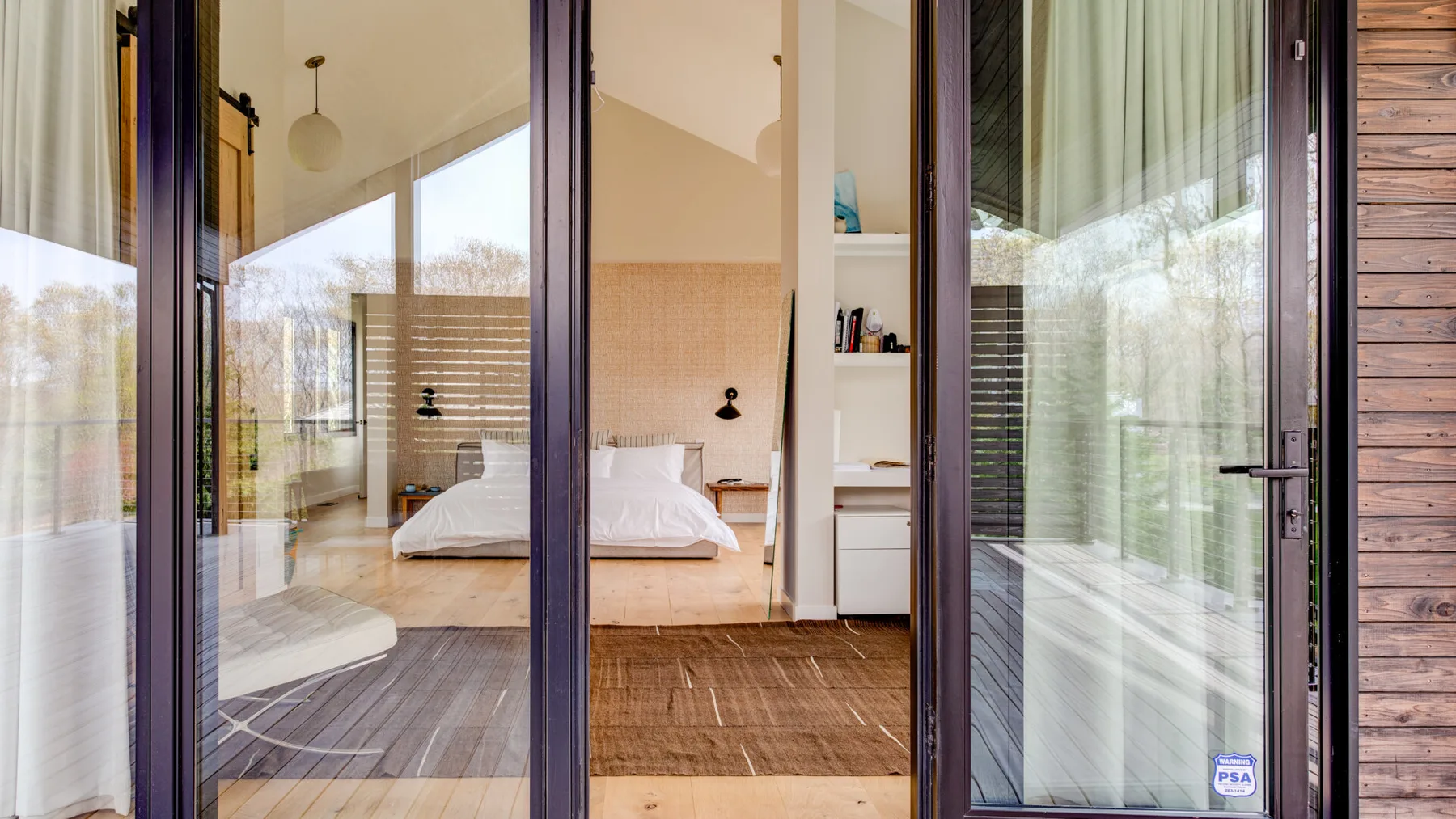 A bedroom with a bed, wooden flooring, and large glass doors opening onto a patio.