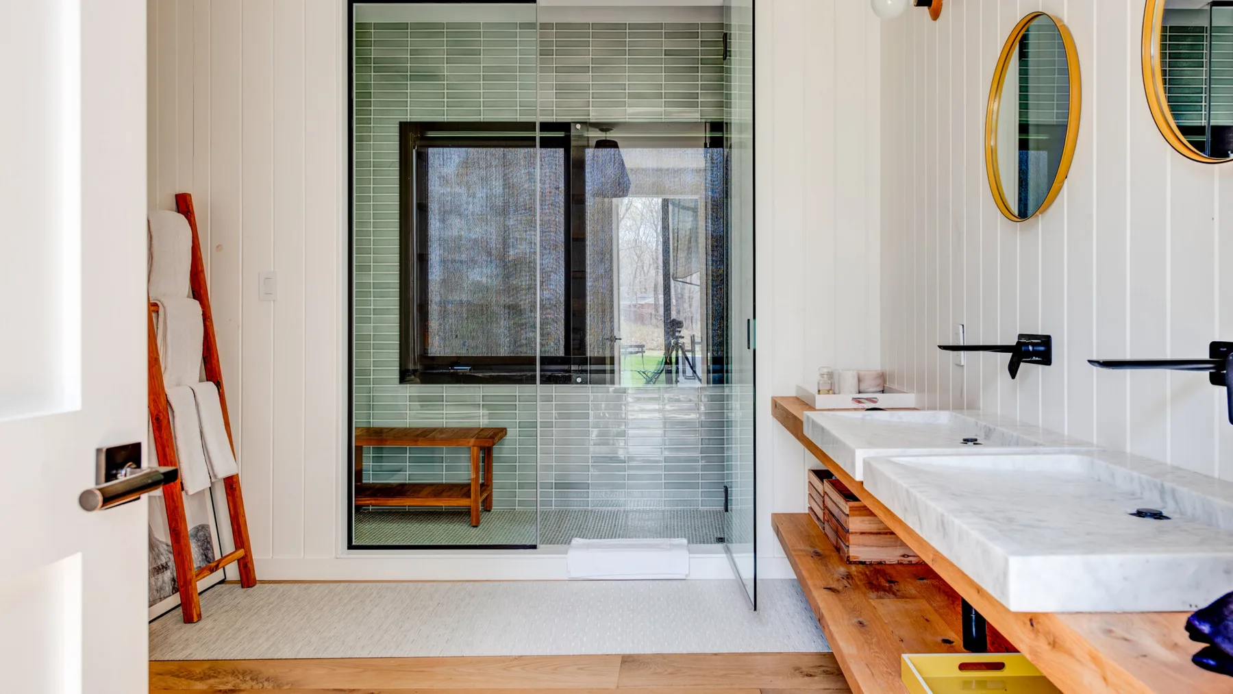 A bathroom with a glass shower, tiled walls, and a long double vanity.