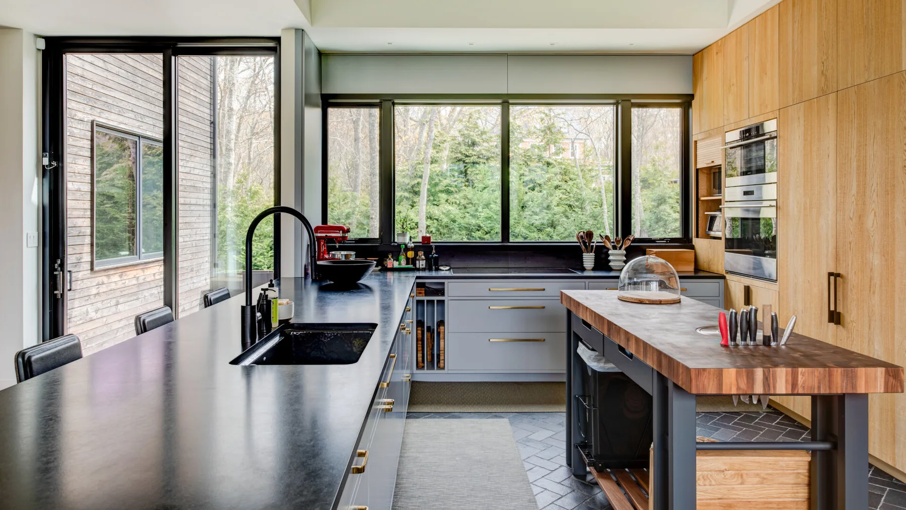 A modern kitchen with dark countertops, wood cabinets, and large windows.
