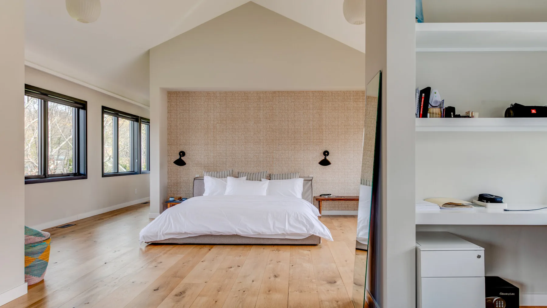 A bright bedroom with a large bed, woven headboard, and windows along one wall.