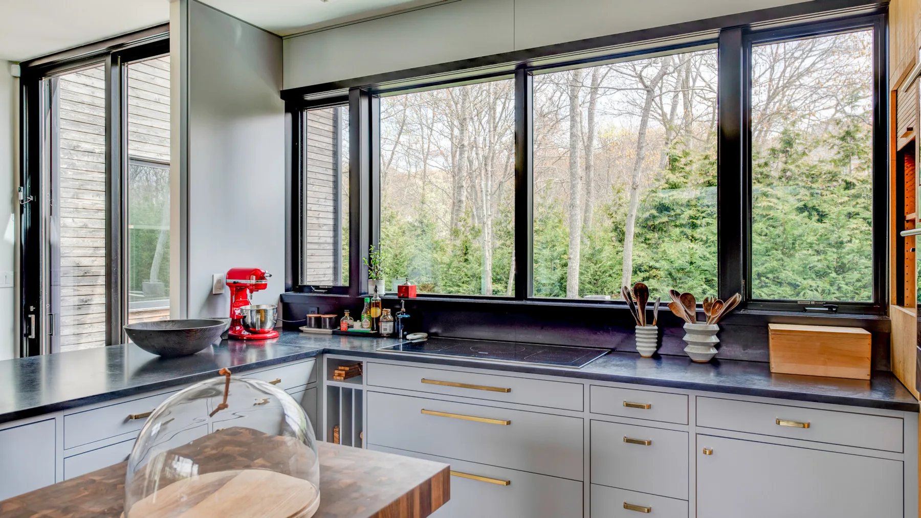A bright kitchen with wide windows overlooking trees and greenery.