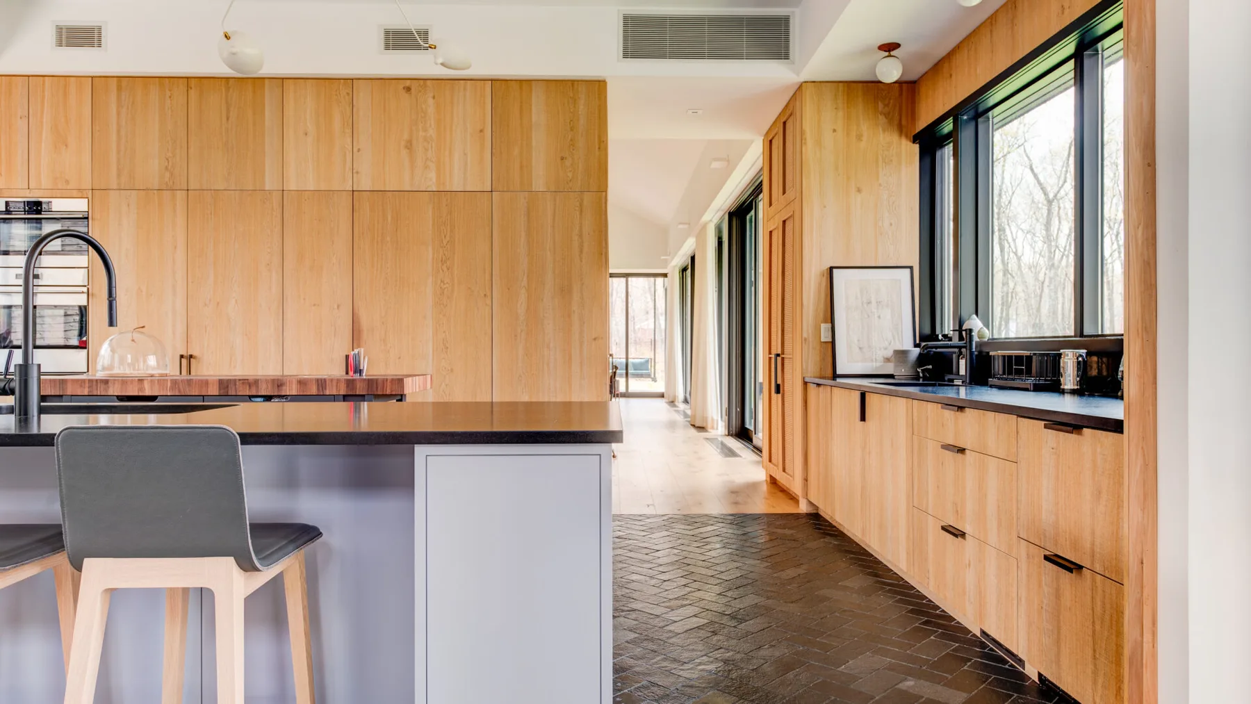 A modern kitchen with wood cabinetry, a central island, and large windows.
