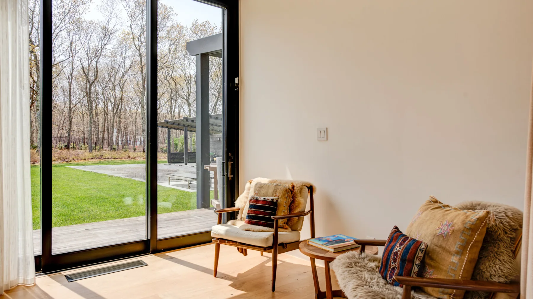 A sitting area beside tall glass doors overlooks a lawn and trees.