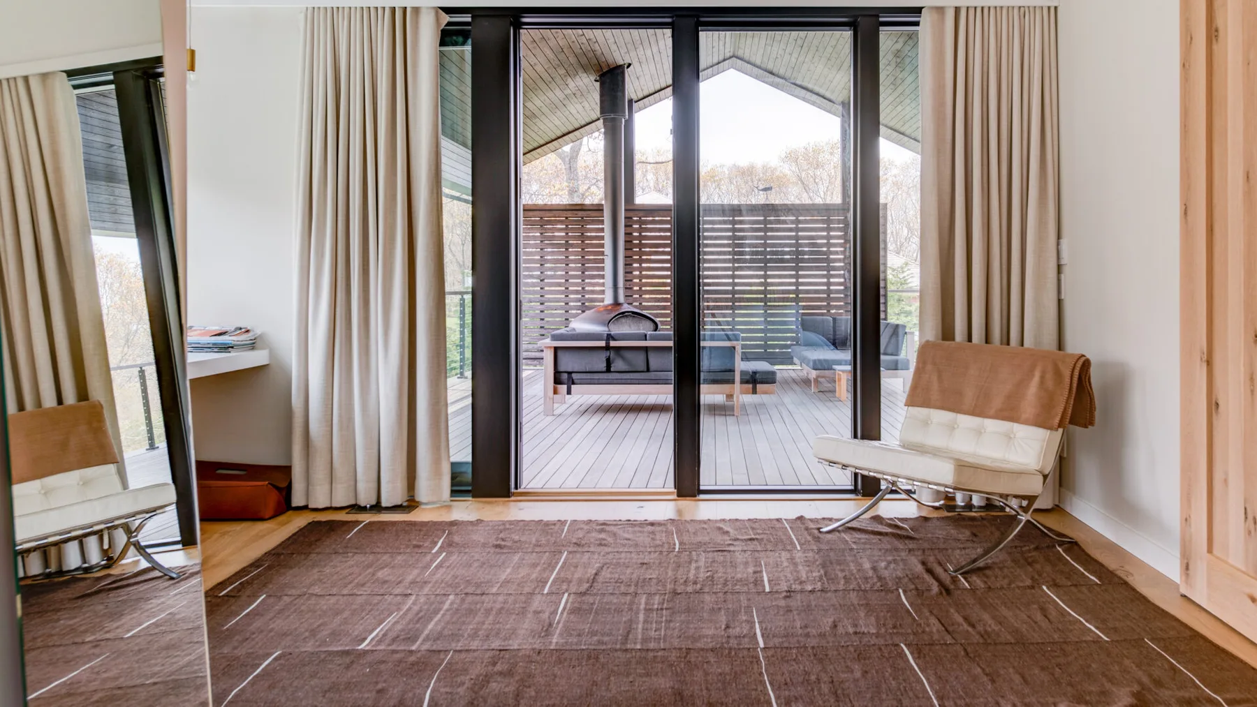 A bright living room opens onto a furnished outdoor deck through large glass doors.