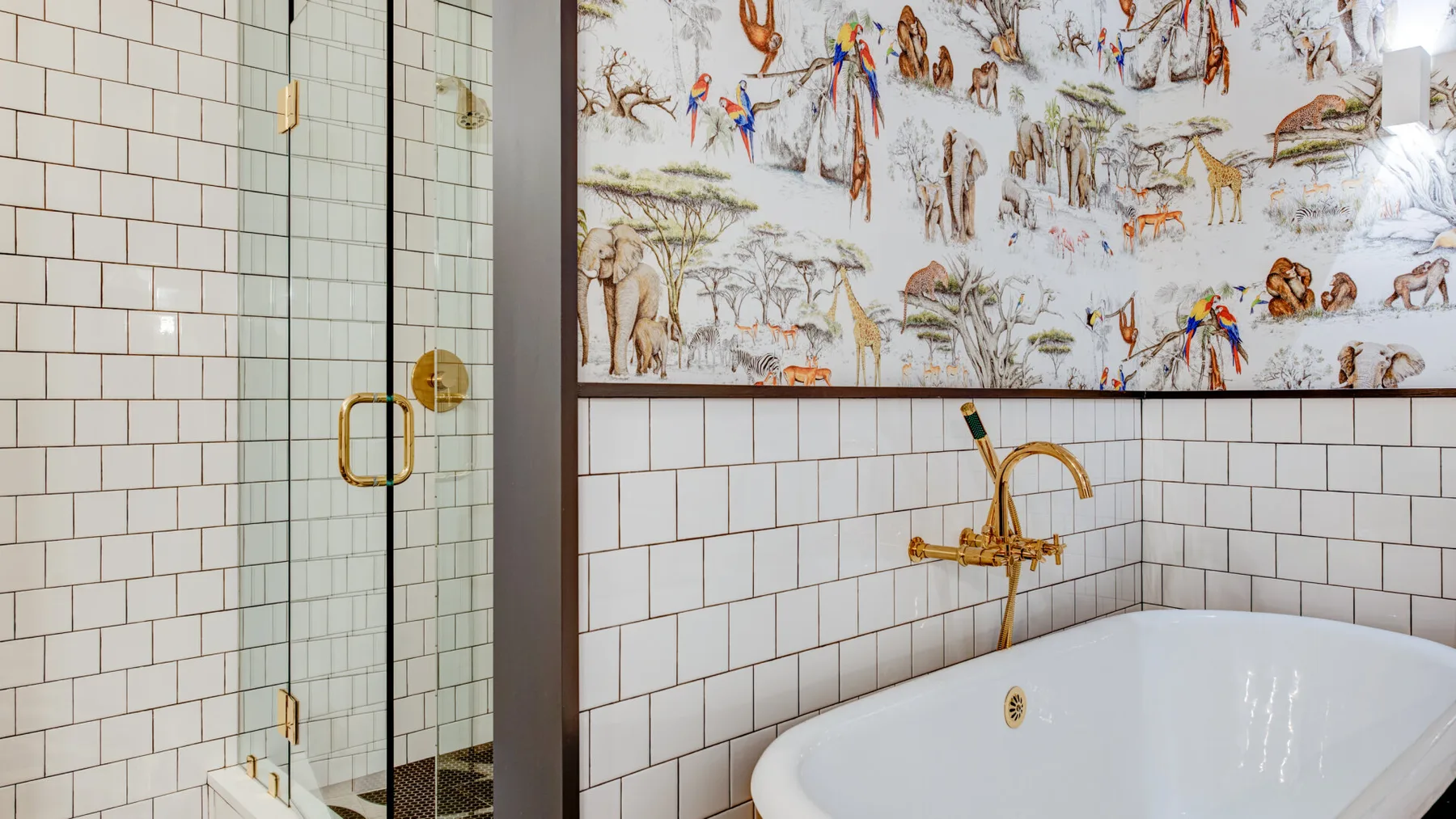 A bathroom with a glass shower and a white bathtub beneath illustrated wall art.