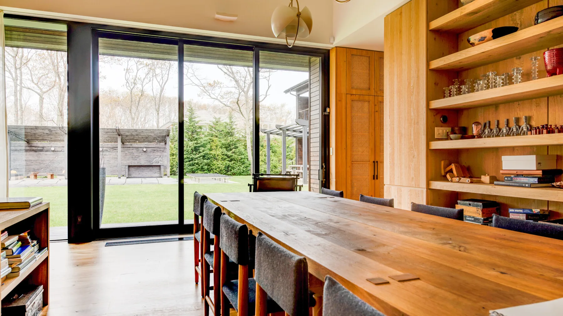 A dining area with a long wooden table beside large windows.