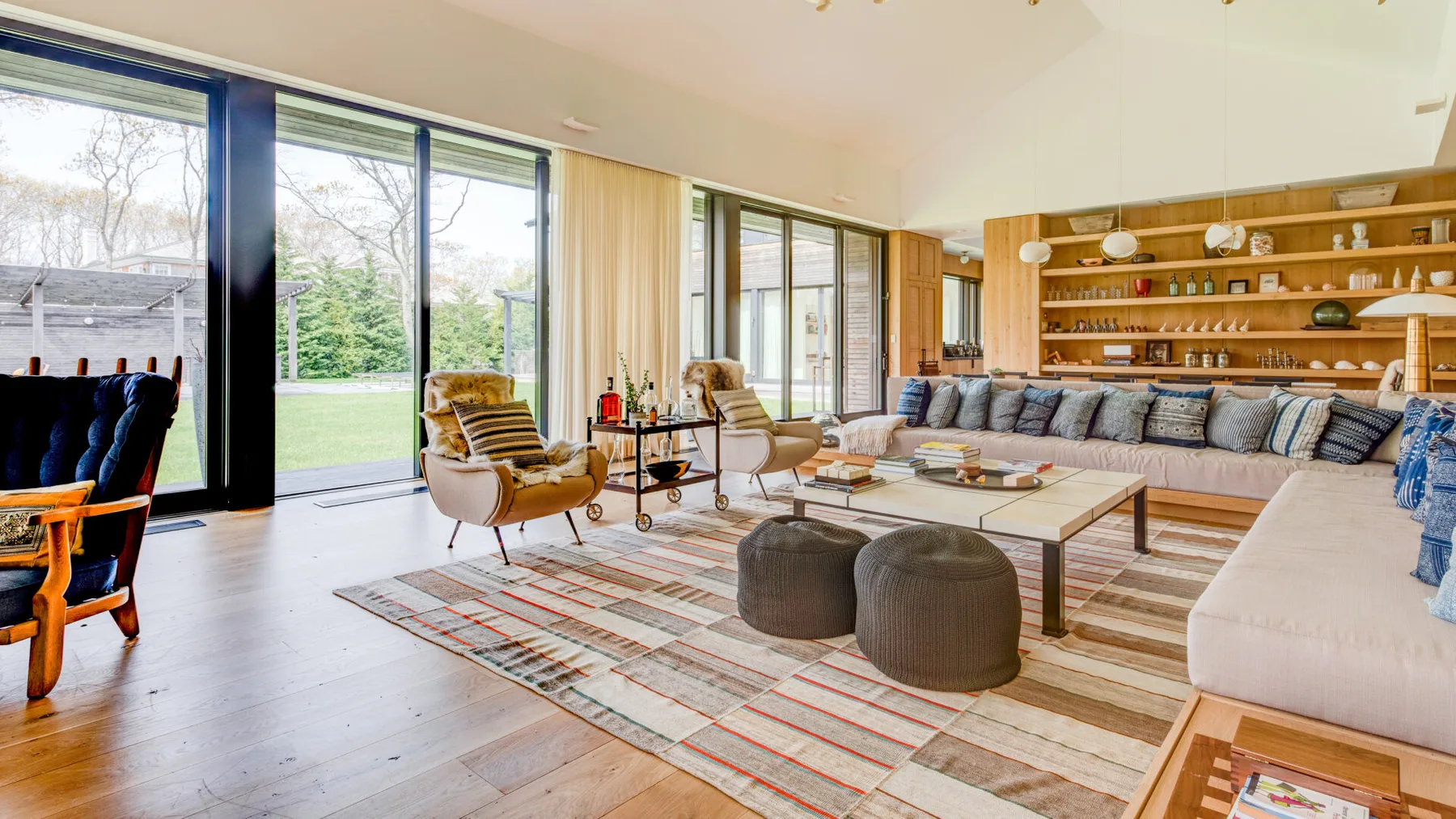 A bright living room with large windows, seating, and a long sofa.