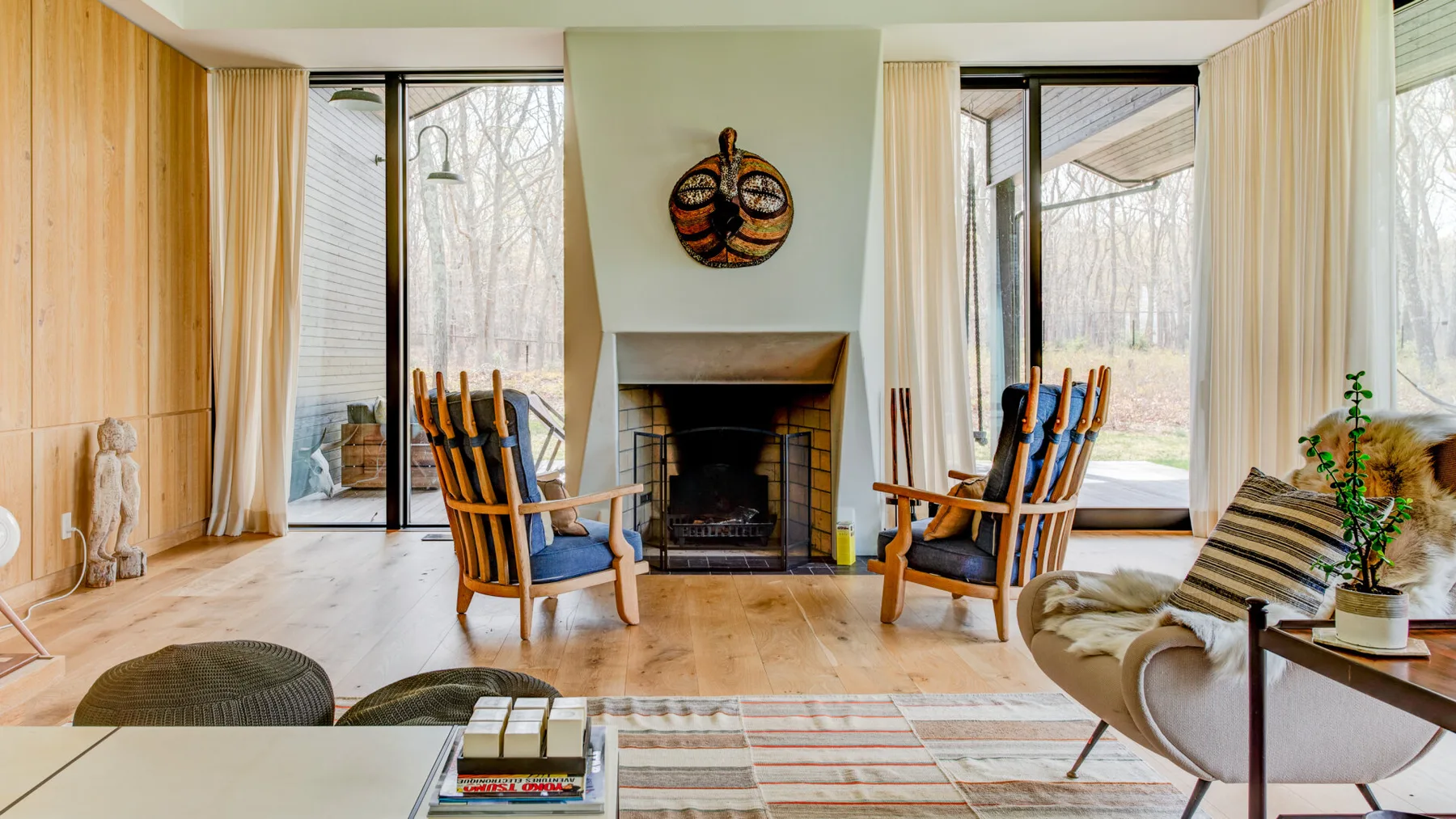 A bright living room has a central fireplace, seating, and large windows.