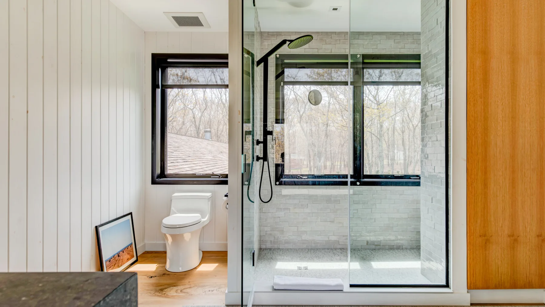 A bathroom with a toilet beside a glass shower and windows.