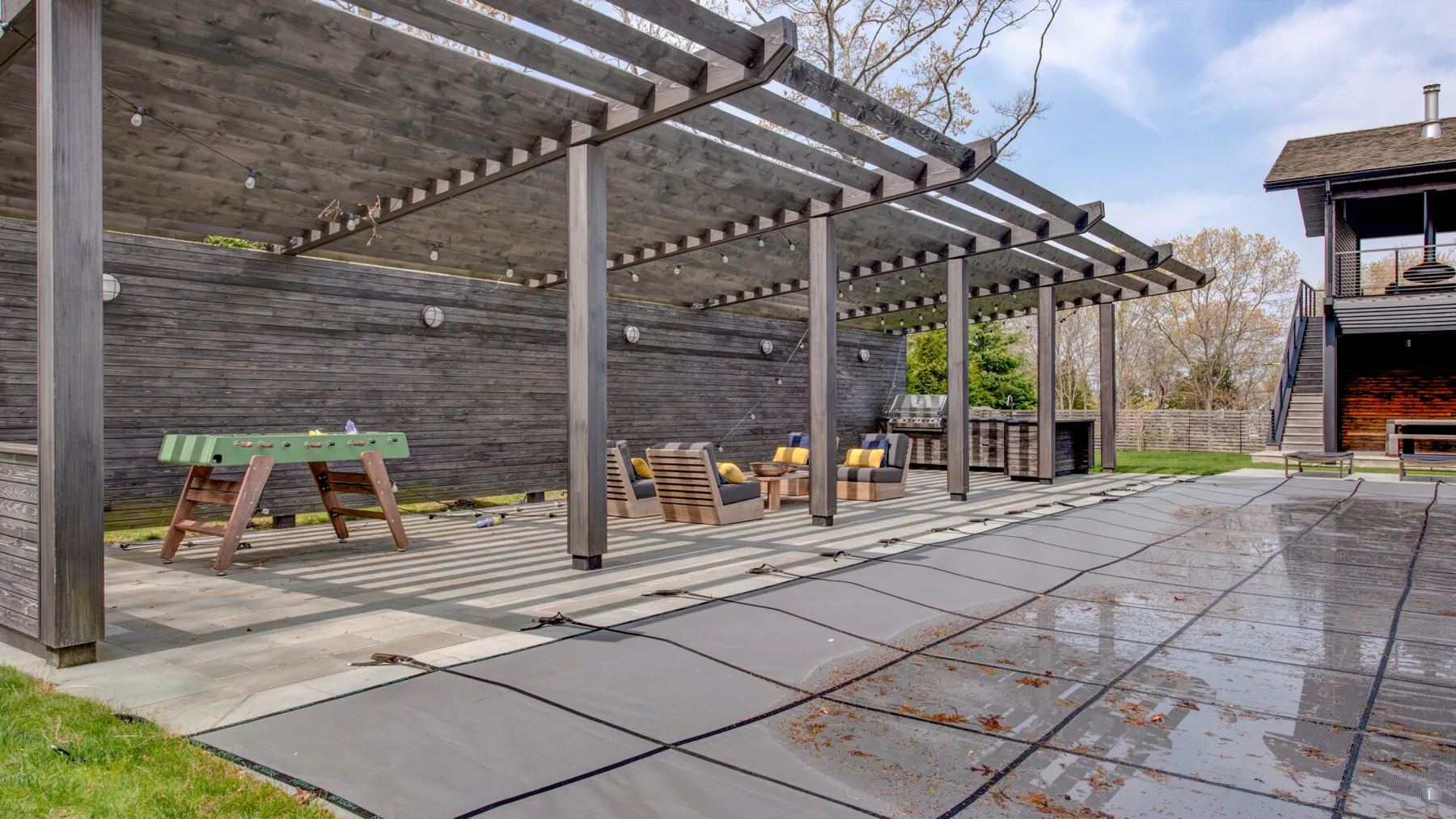 An outdoor patio beneath a wooden pergola, with a picnic table nearby.