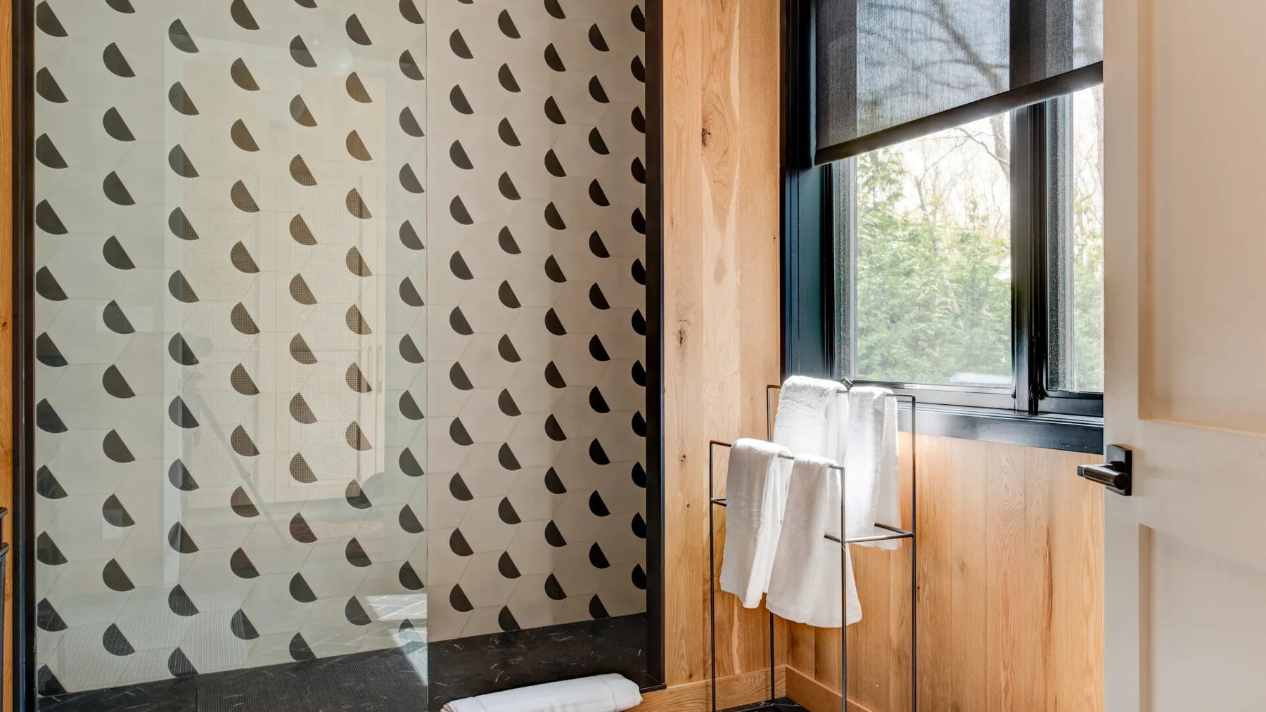 A bathroom shower area with patterned wall tiles and a large window.