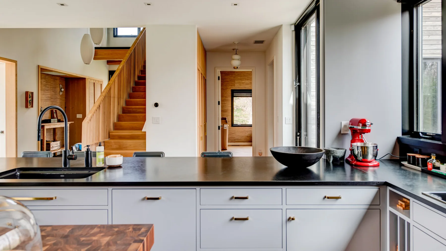 A kitchen with a dark countertop and a staircase beyond it.