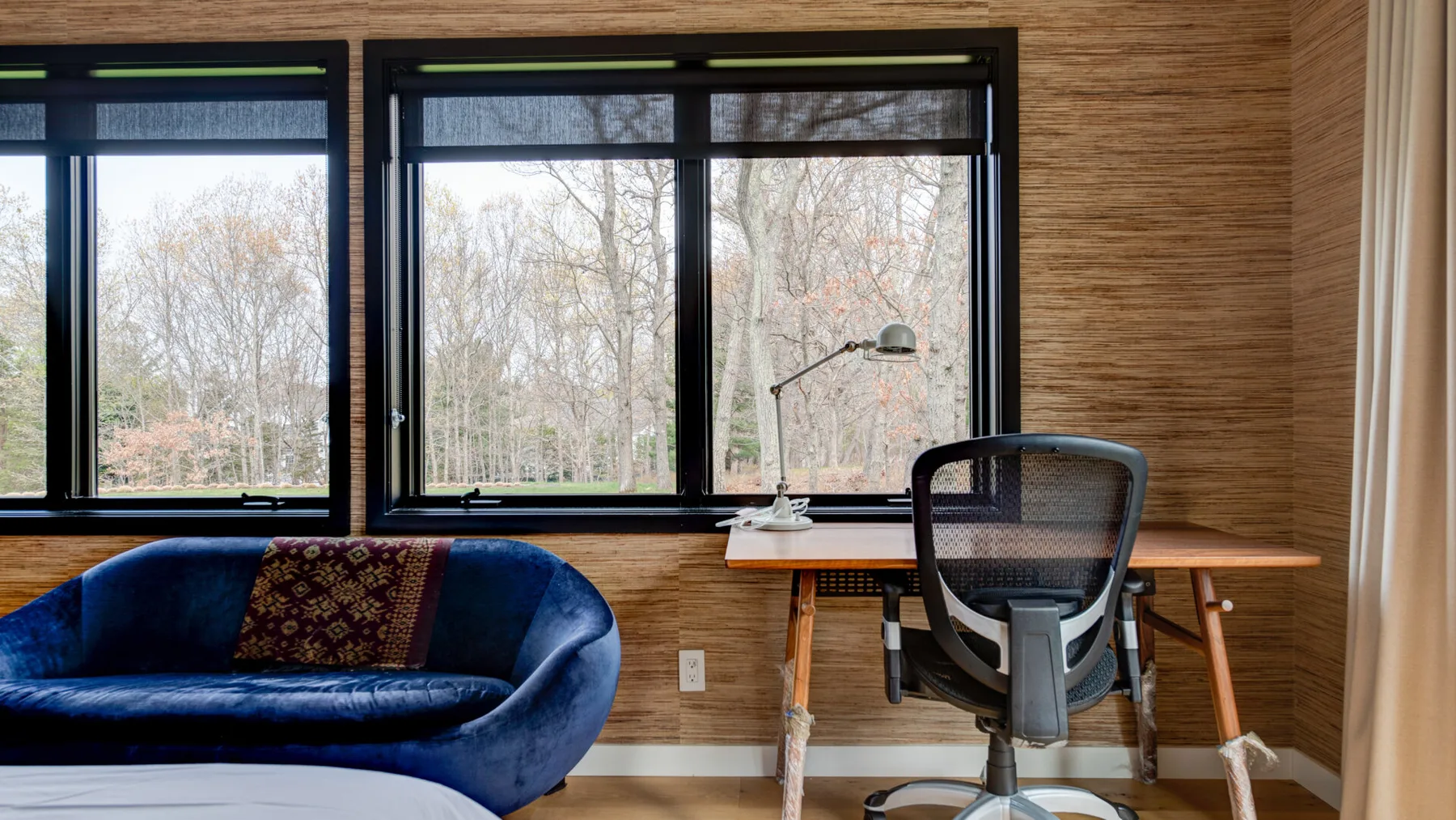 A sitting area with a blue sofa, desk, and large windows.
