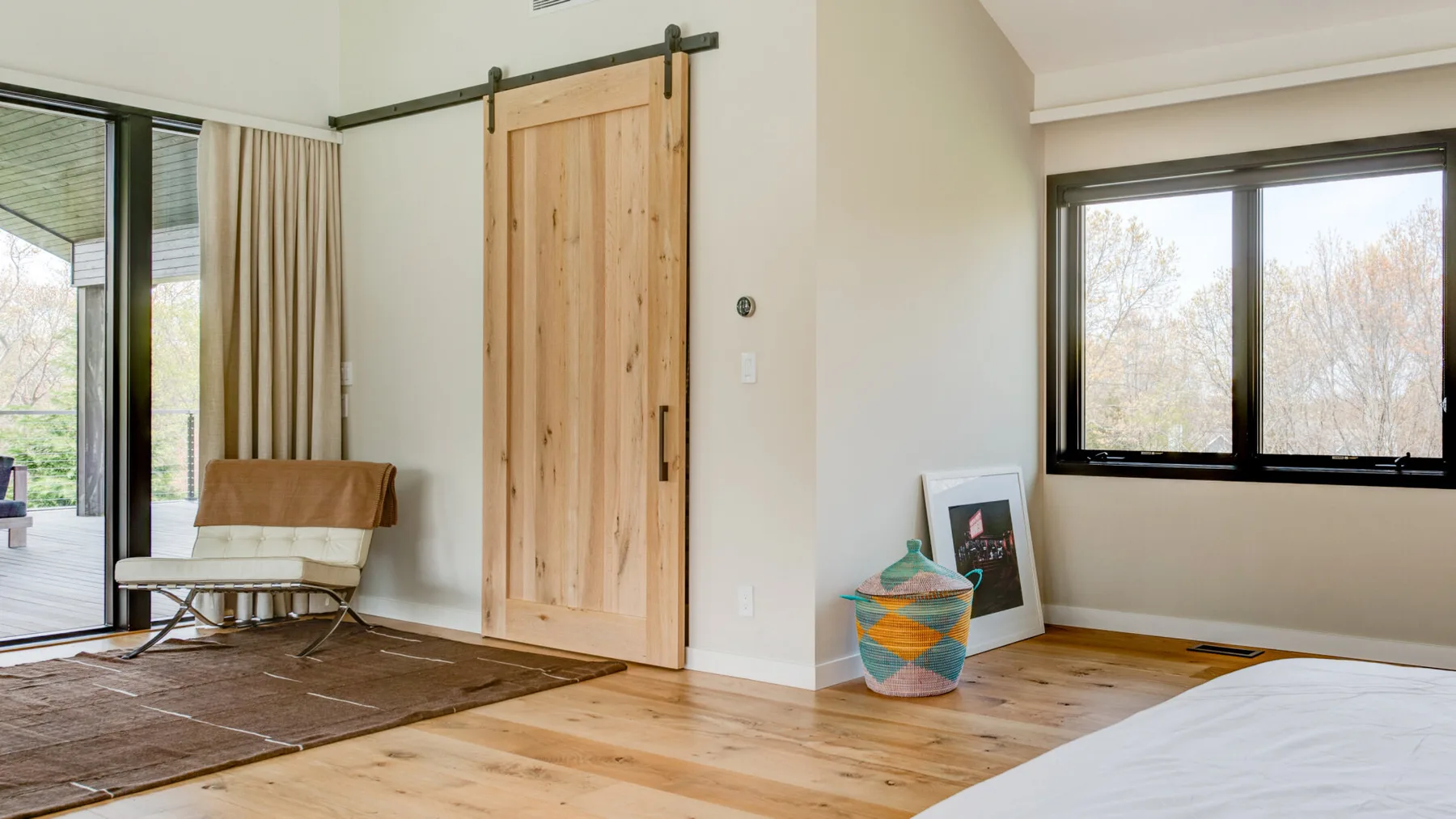 A bright room with a wooden sliding door, large windows, and a bed.