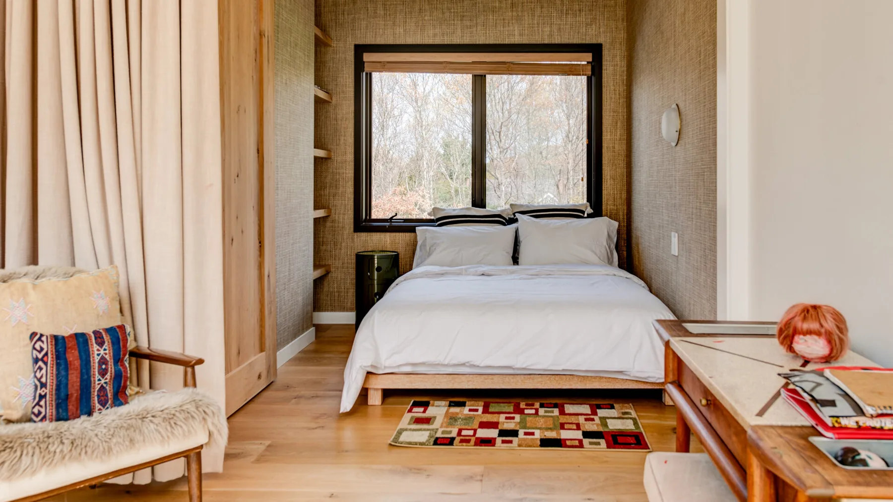 A bedroom with a bed beneath a large window and a small patterned rug.