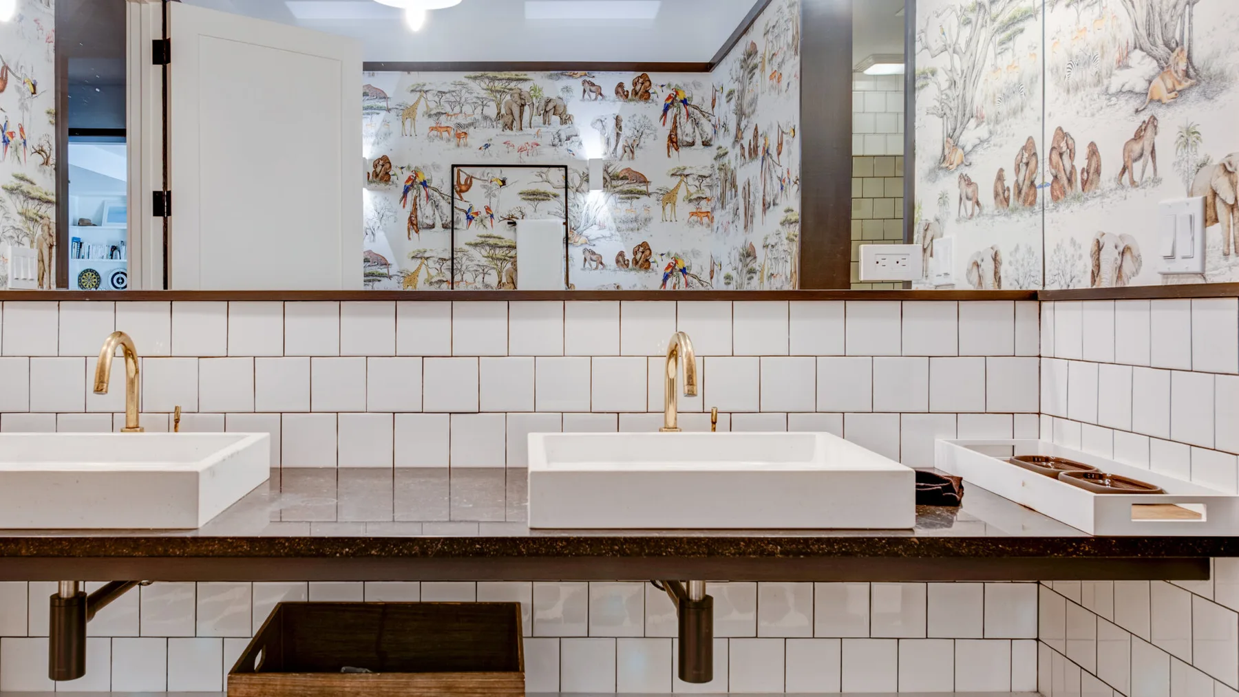 A bathroom vanity with two sinks, tiled walls, and illustrated wallpaper.