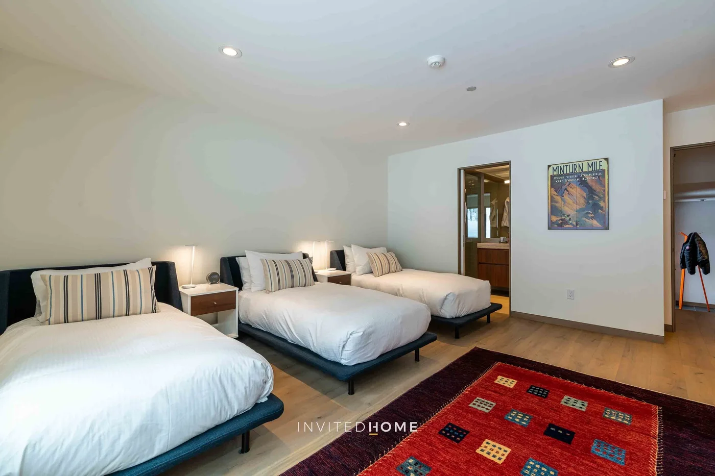 Un dormitorio con varias camas, ropa de cama blanca y una alfombra roja estampada.