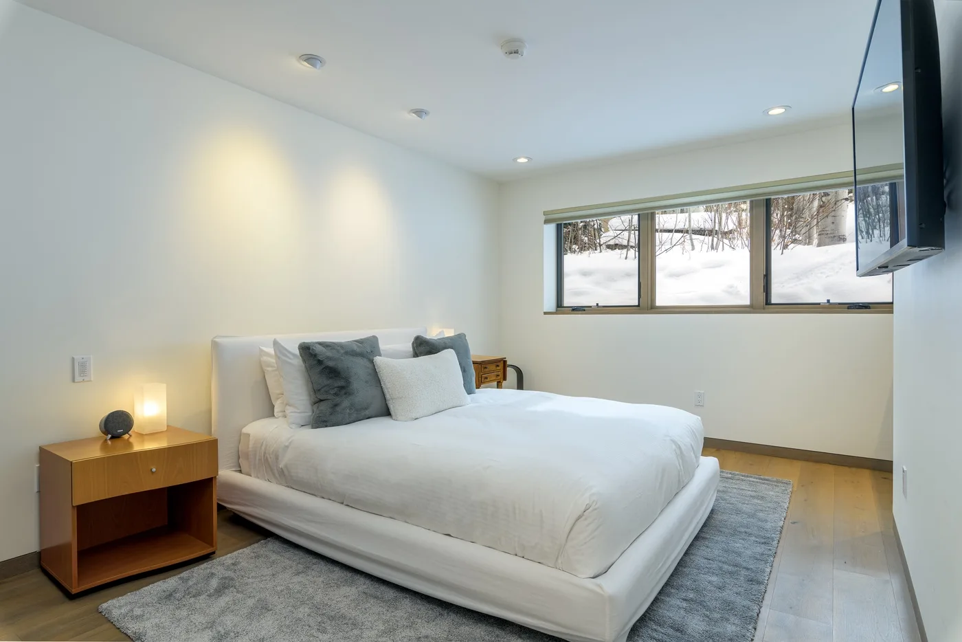 Un dormitorio luminoso con una cama blanca, una mesita de noche y una ventana.
