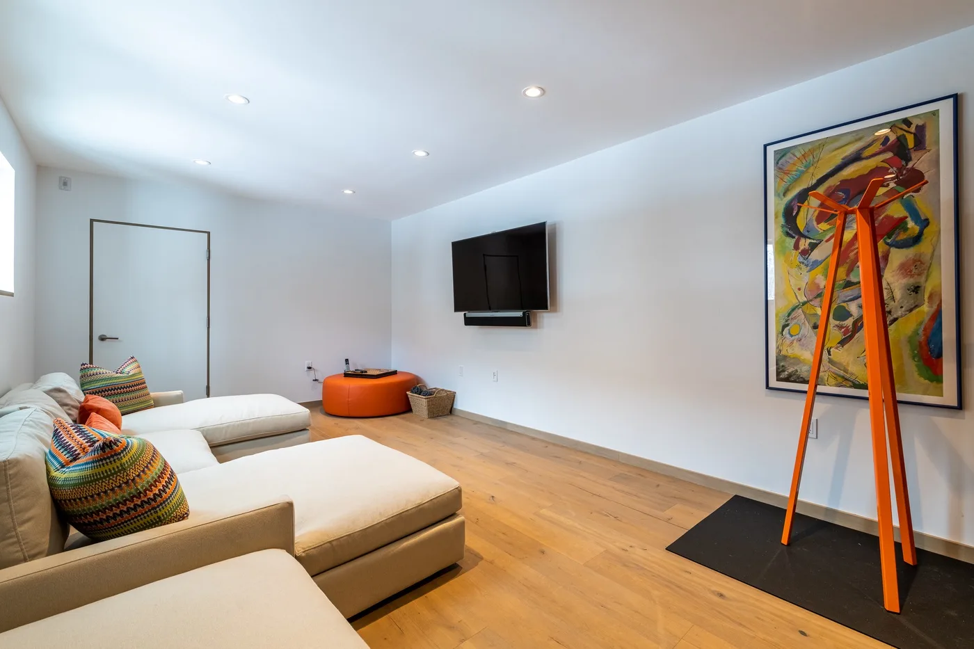 Una sala luminosa con asientos claros, un televisor en la pared y arte colorido.