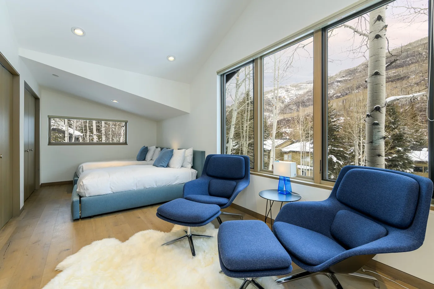 Un dormitorio luminoso con una cama y asientos azules junto a grandes ventanas.