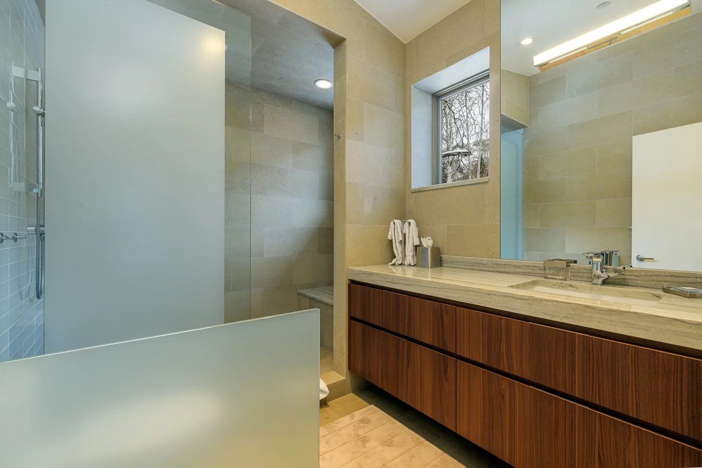 Un baño alicatado con una ducha de vidrio y un tocador largo.