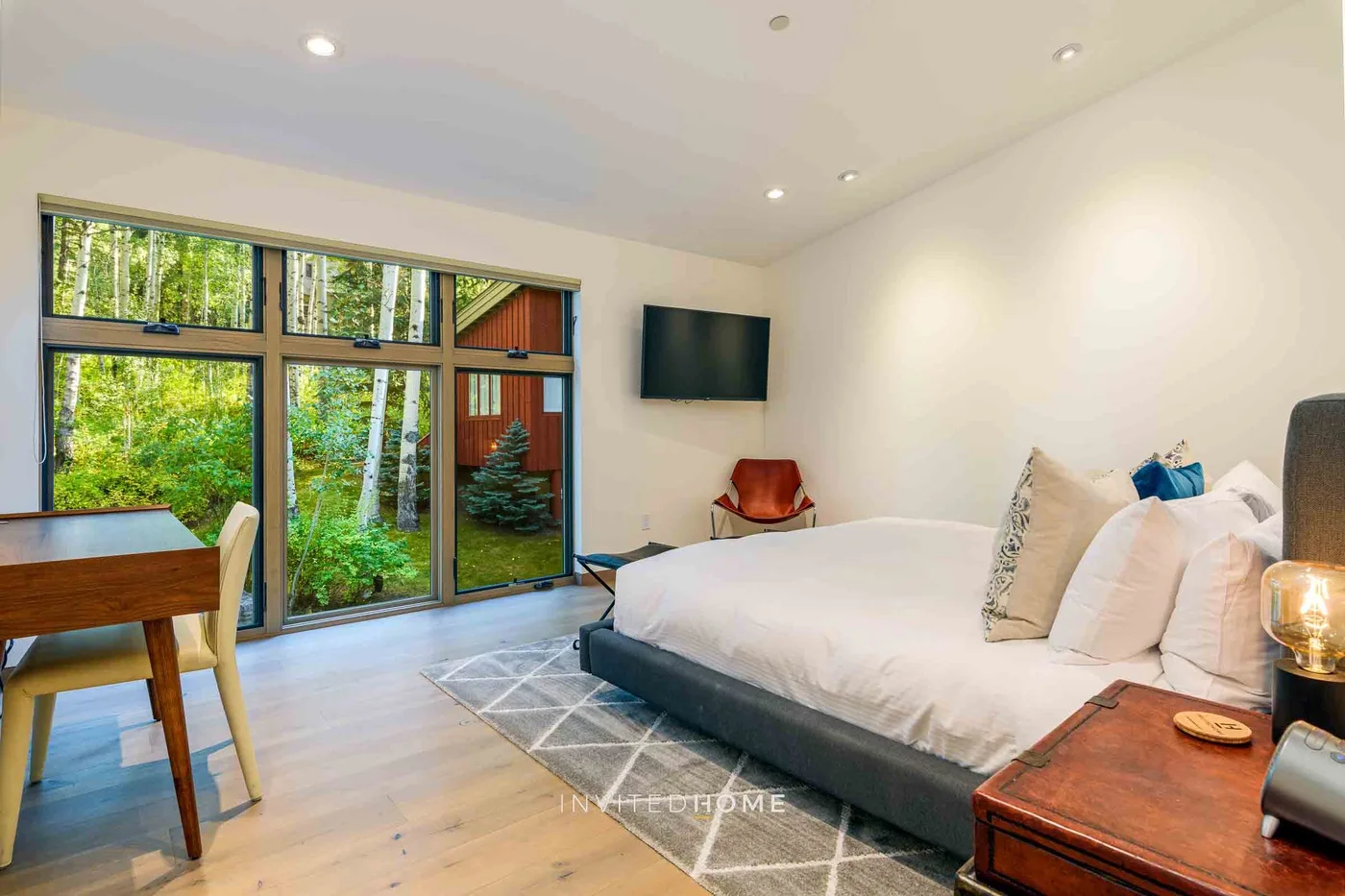 Un dormitorio con una cama grande, un escritorio y ventanas con vistas a la vegetación.