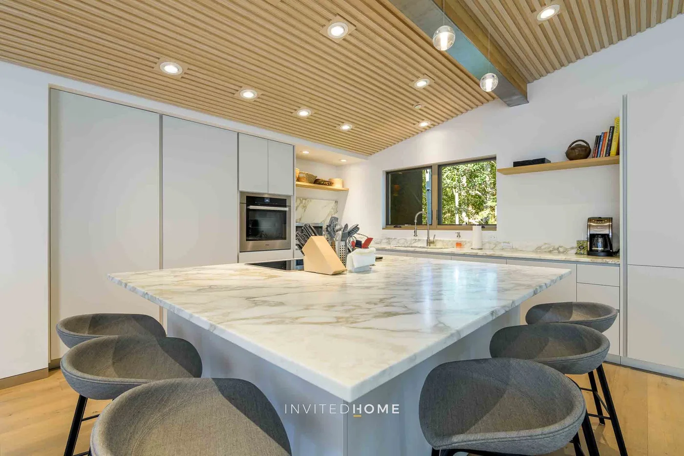 Una cocina moderna y luminosa cuenta con una gran isla con asientos bajo un techo de listones de madera.