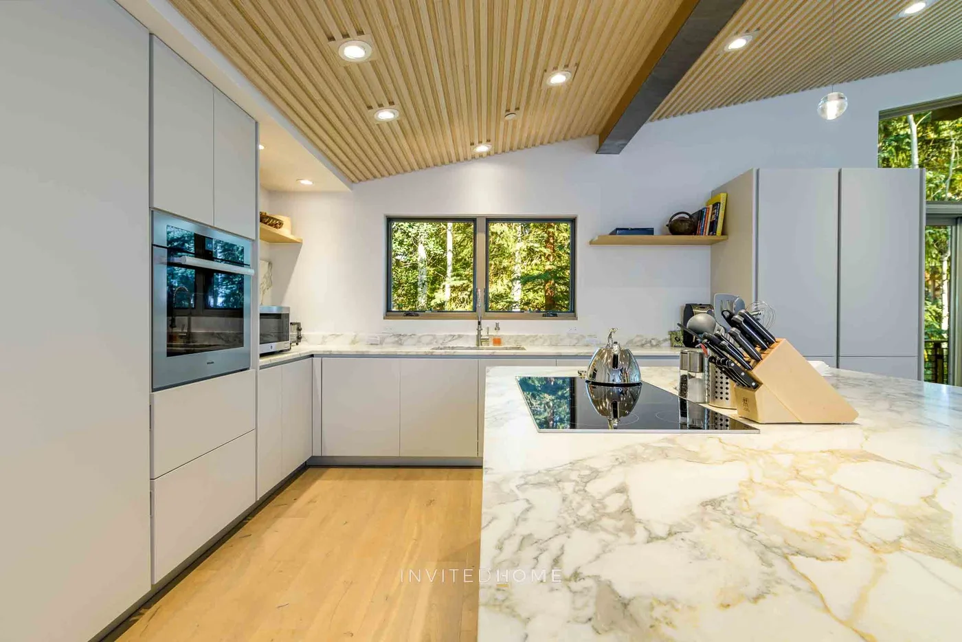 Una cocina moderna con gabinetes claros, una isla amplia y ventanas con vista a la vegetación.