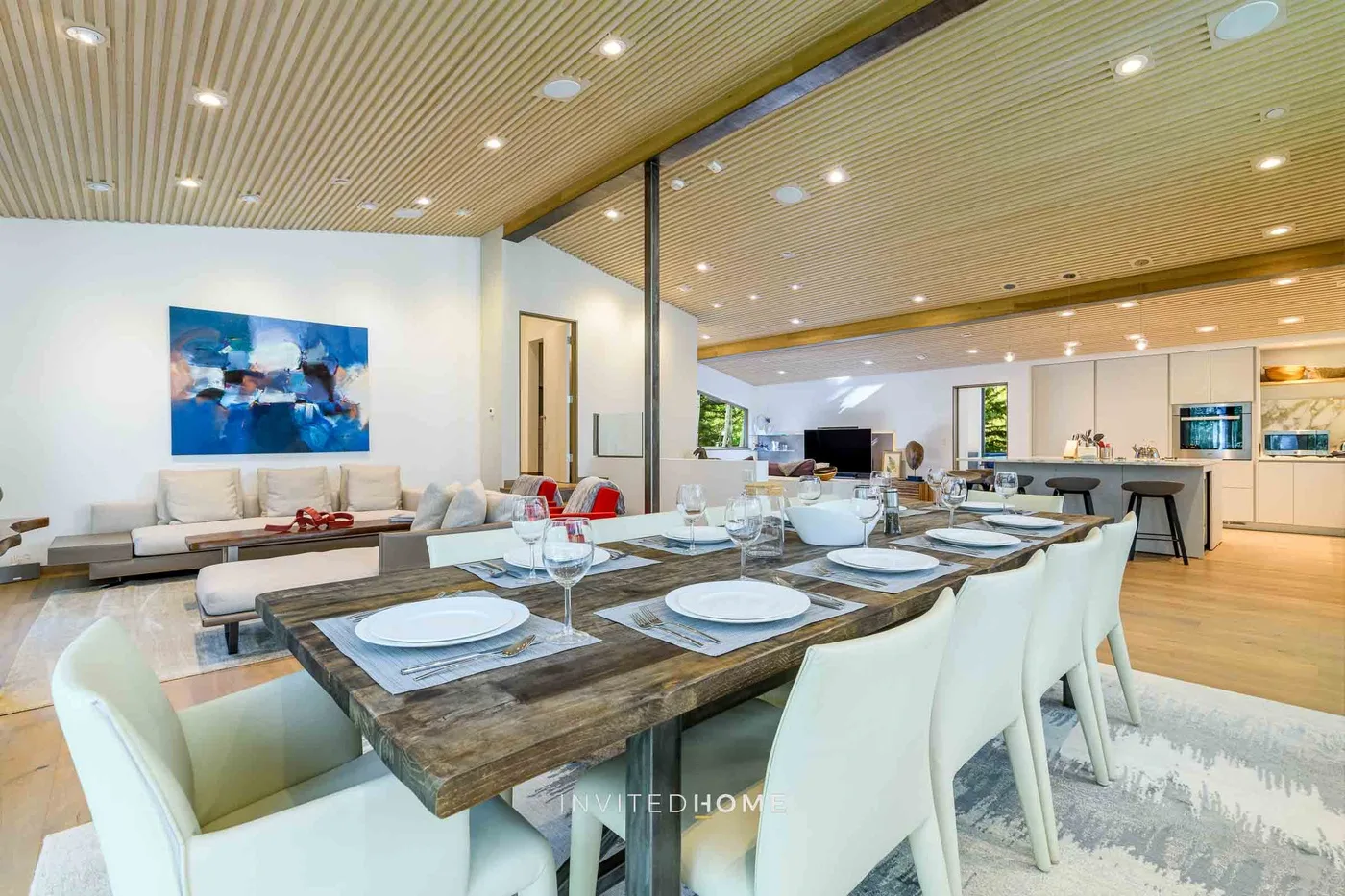 Comedor con una larga mesa de madera con vajilla y rodeada de asientos blancos.