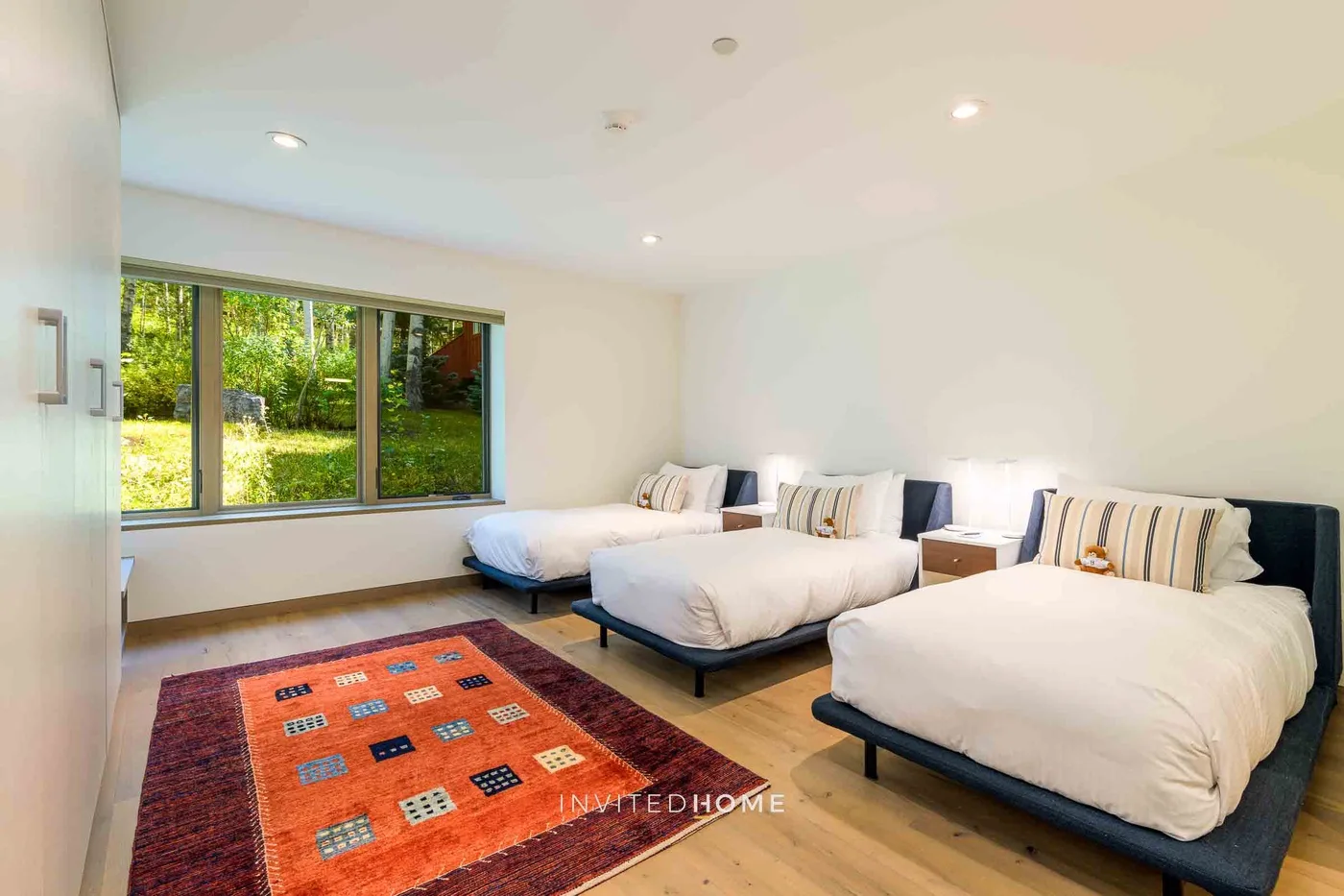 Un dormitorio luminoso con varias camas y una alfombra colorida.