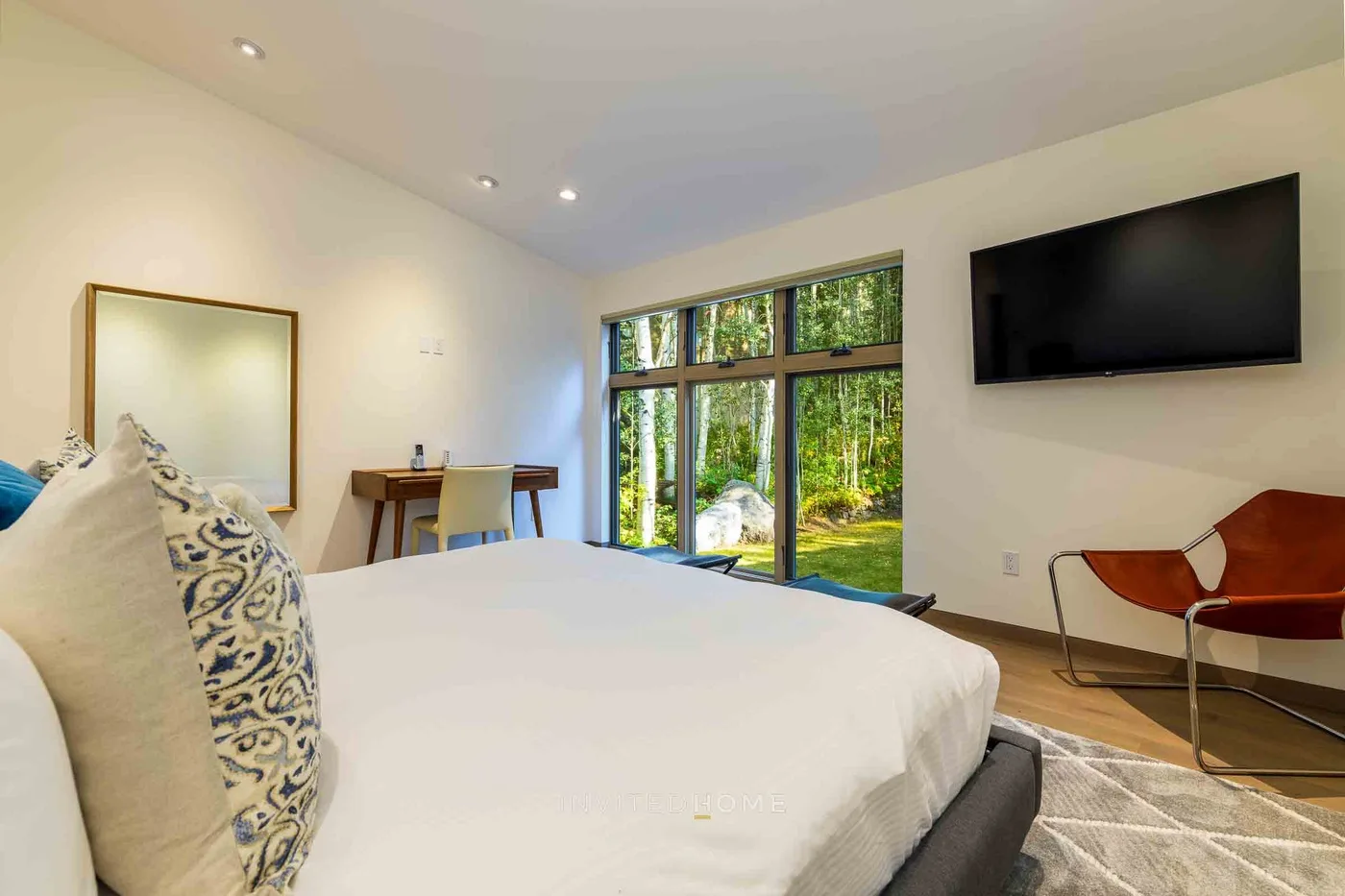 Un dormitorio luminoso con una cama grande, un escritorio y ventanas con vistas a la vegetación.