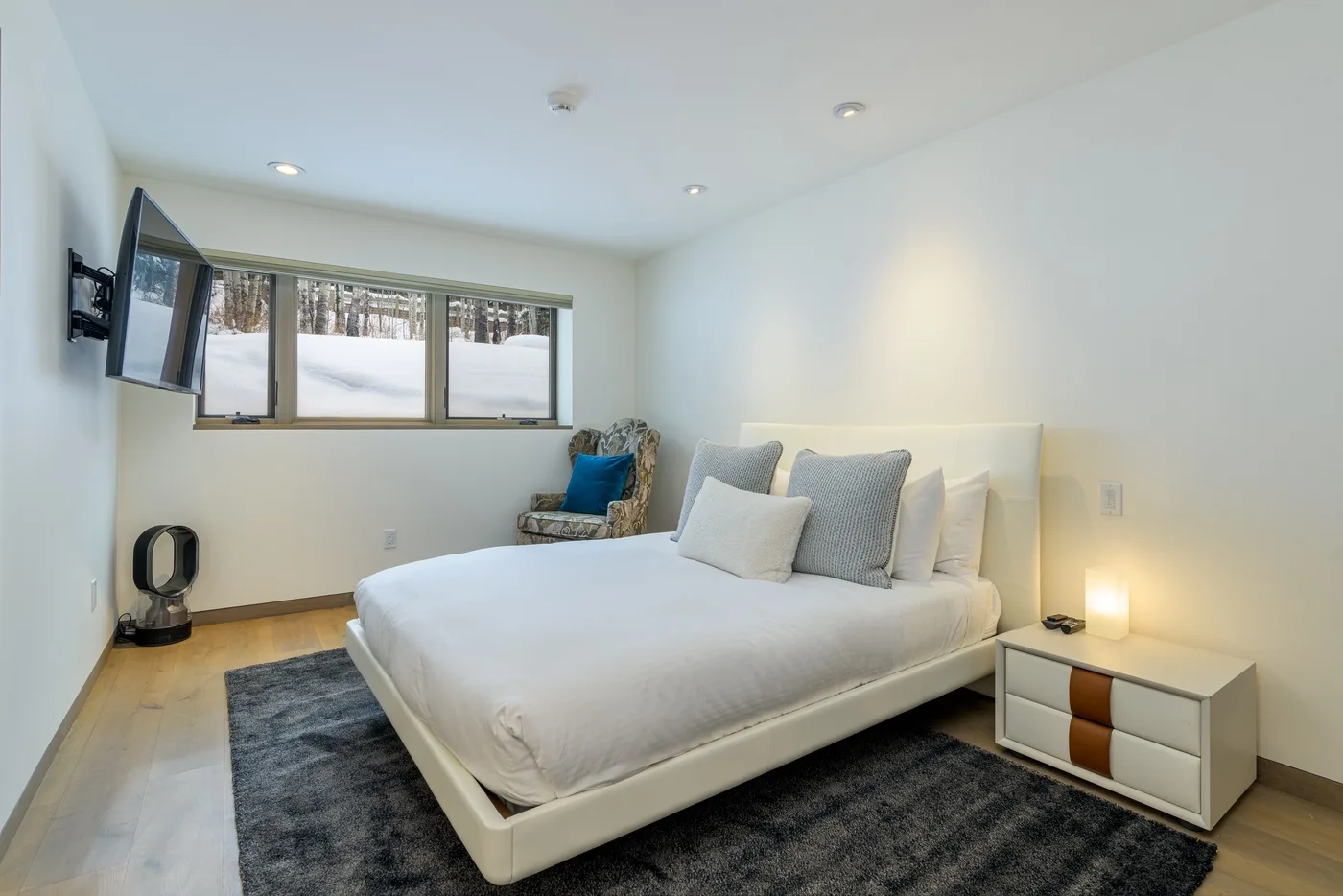 Un dormitorio luminoso con una cama grande, una alfombra oscura y ventanas en la pared.