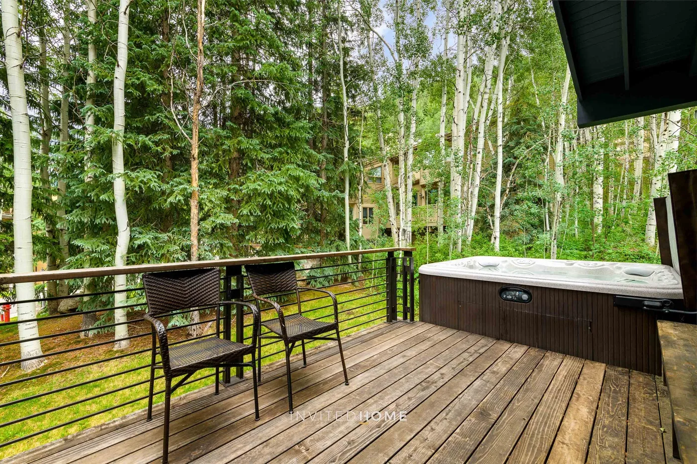 Una terraza de madera da a una zona arbolada, con asientos y una bañera de hidromasaje.