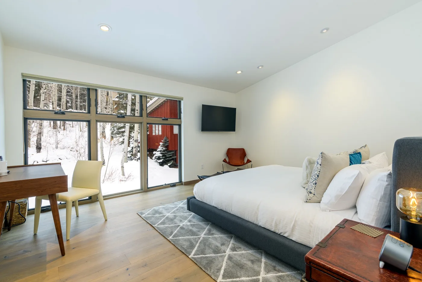 Un dormitorio con una cama grande junto a amplias ventanas con vistas a un paisaje nevado.