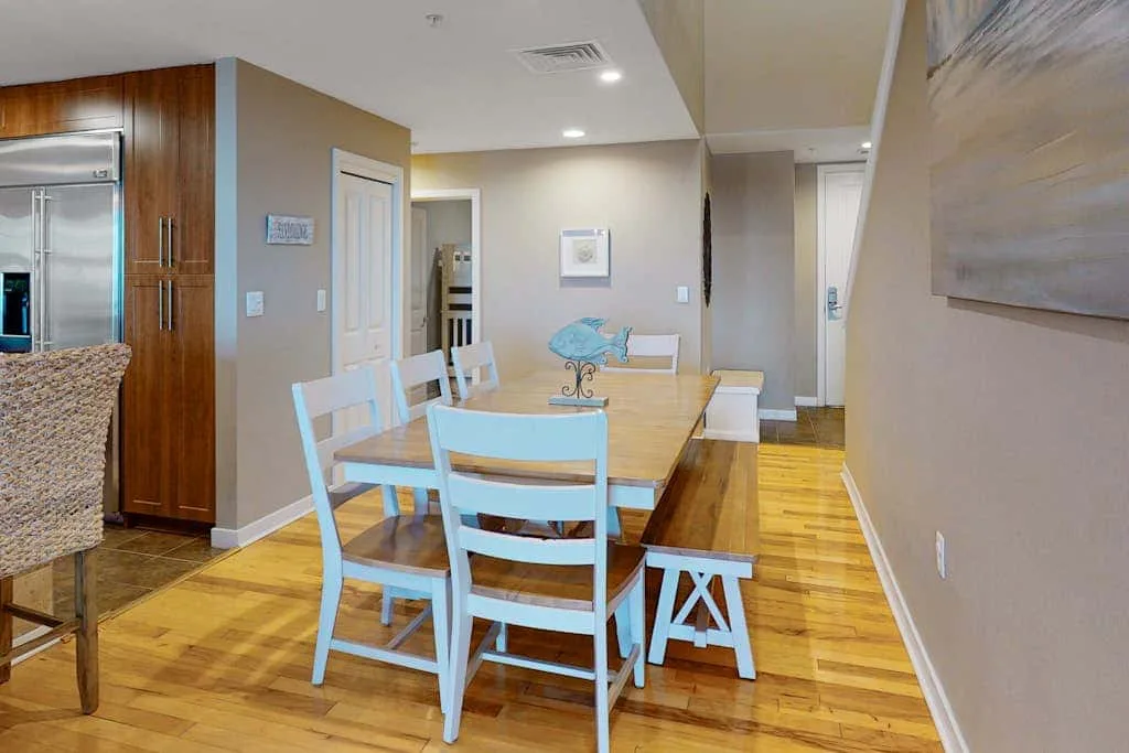 Un comedor con una mesa de madera y sillas blancas junto a la cocina.