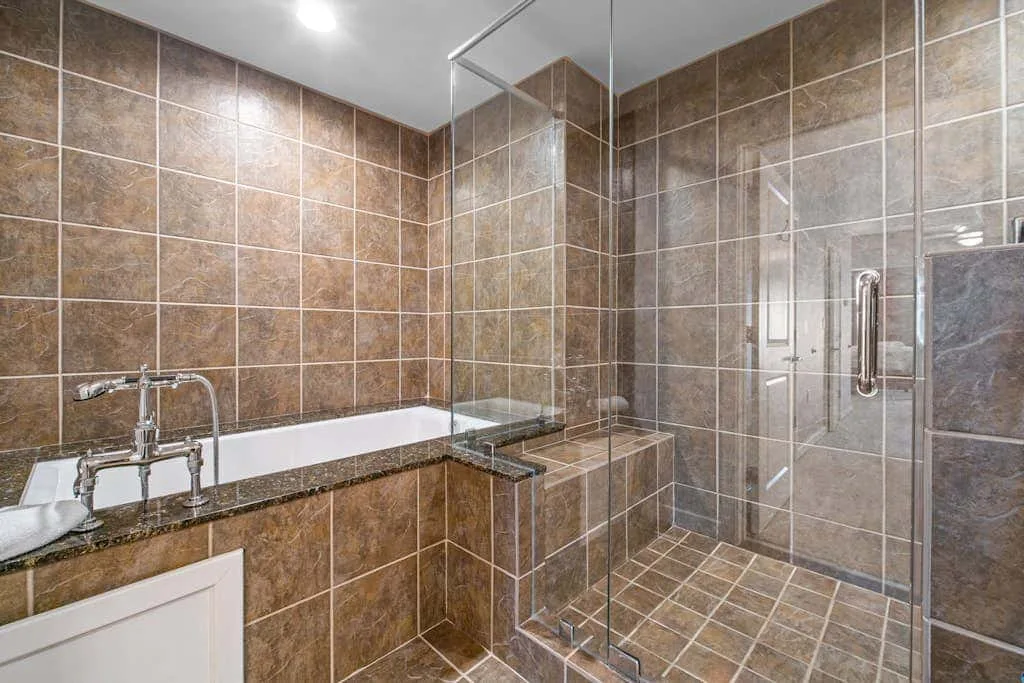Un baño revestido de azulejos con bañera y ducha de vidrio.
