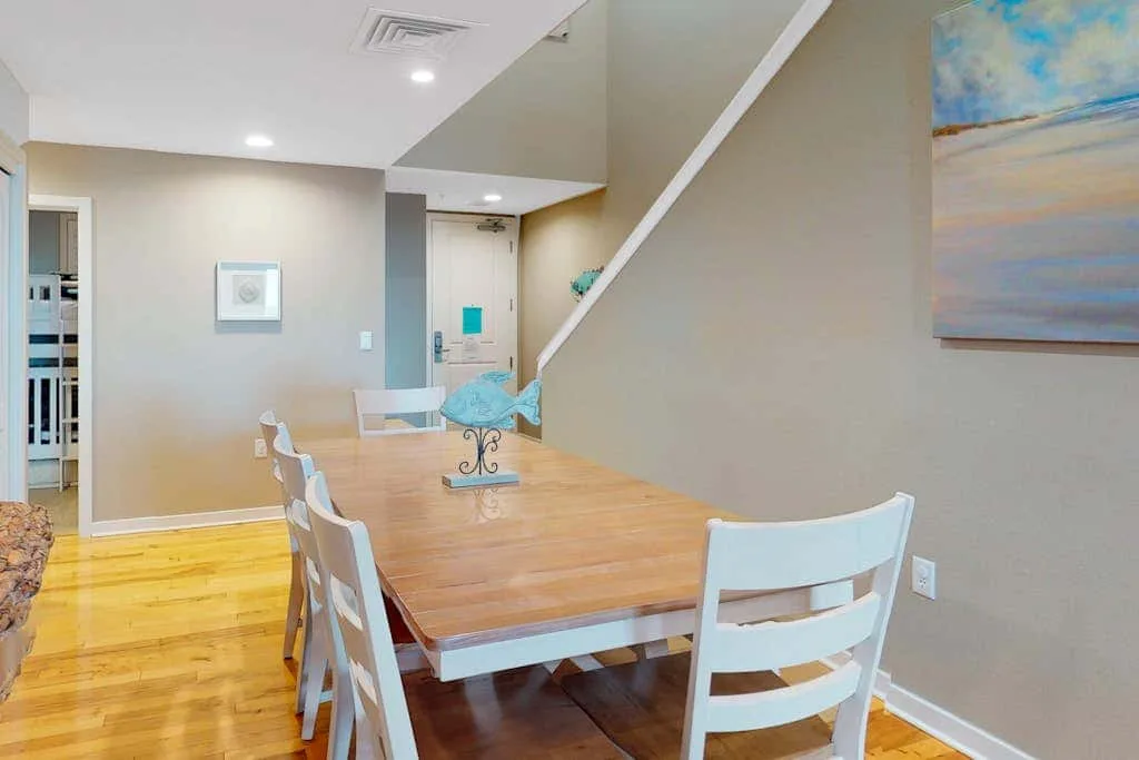 Un comedor con una mesa de madera, sillas blancas y una escalera.