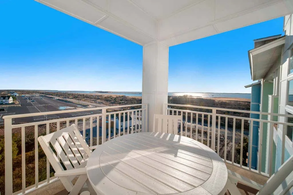 A covered balcony with white seating overlooks a broad coastal landscape.