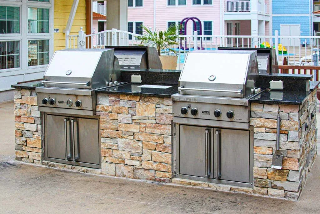 Una zona de parrillas al aire libre con parrillas de acero inoxidable en una encimera de piedra.