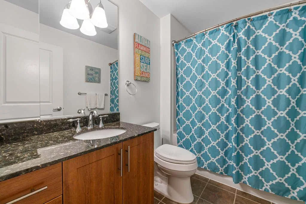 Un baño con lavabo, espejo, inodoro y cortina de ducha azul estampada.