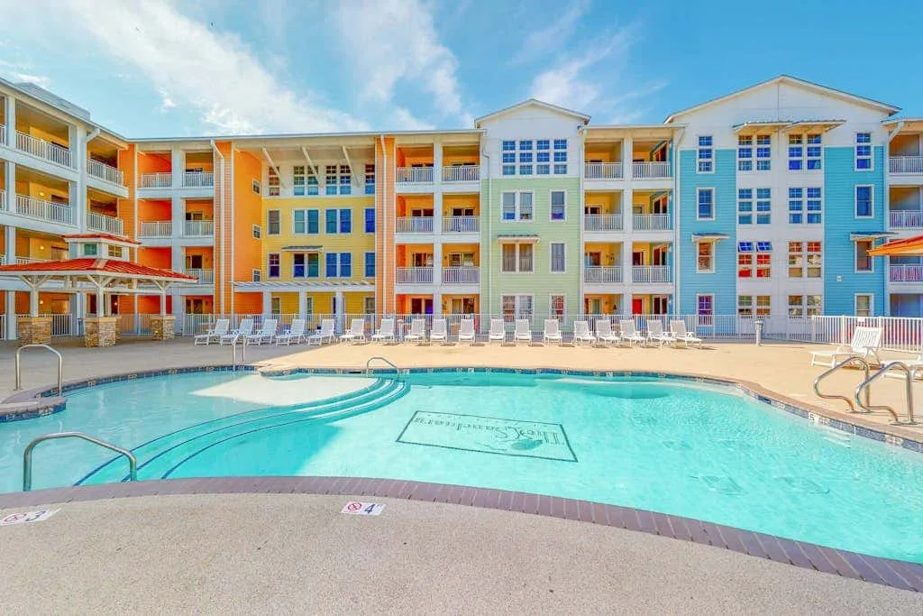 Una piscina al aire libre está frente a un edificio colorido de varios pisos.