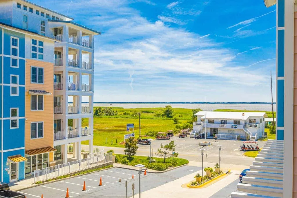 Una vista costera muestra edificios modernos junto a una zona verde abierta y un cielo azul.