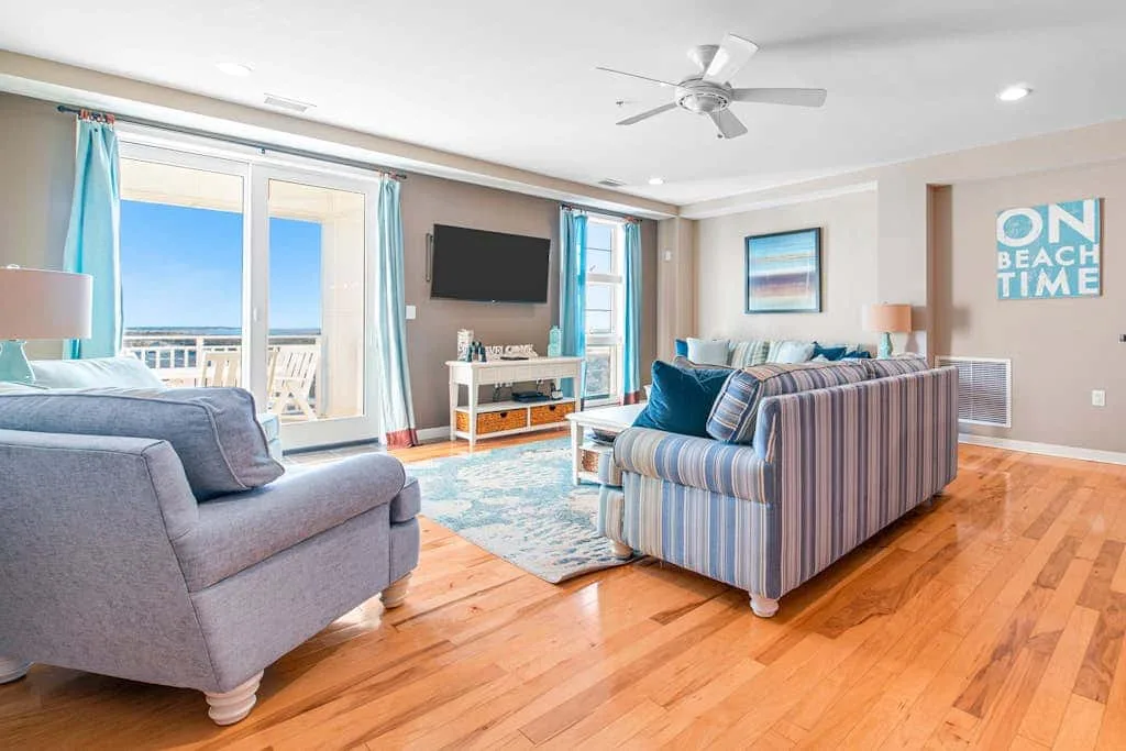 A bright living room with seating, a wall-mounted television, and glass doors opening onto a balcony.
